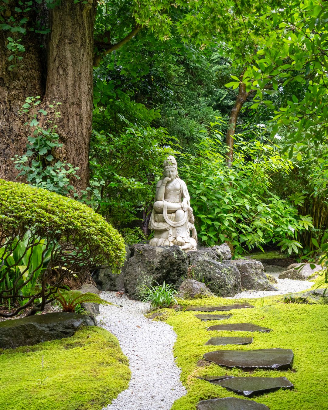 A stone figure on moss beside a gravel path in a Japanese garden