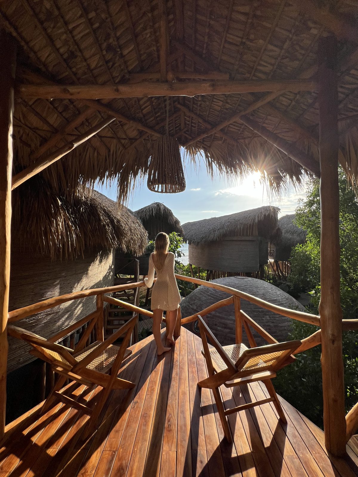 A guest on a private deck at sunset, looking out over the thatched roofs to the ocean