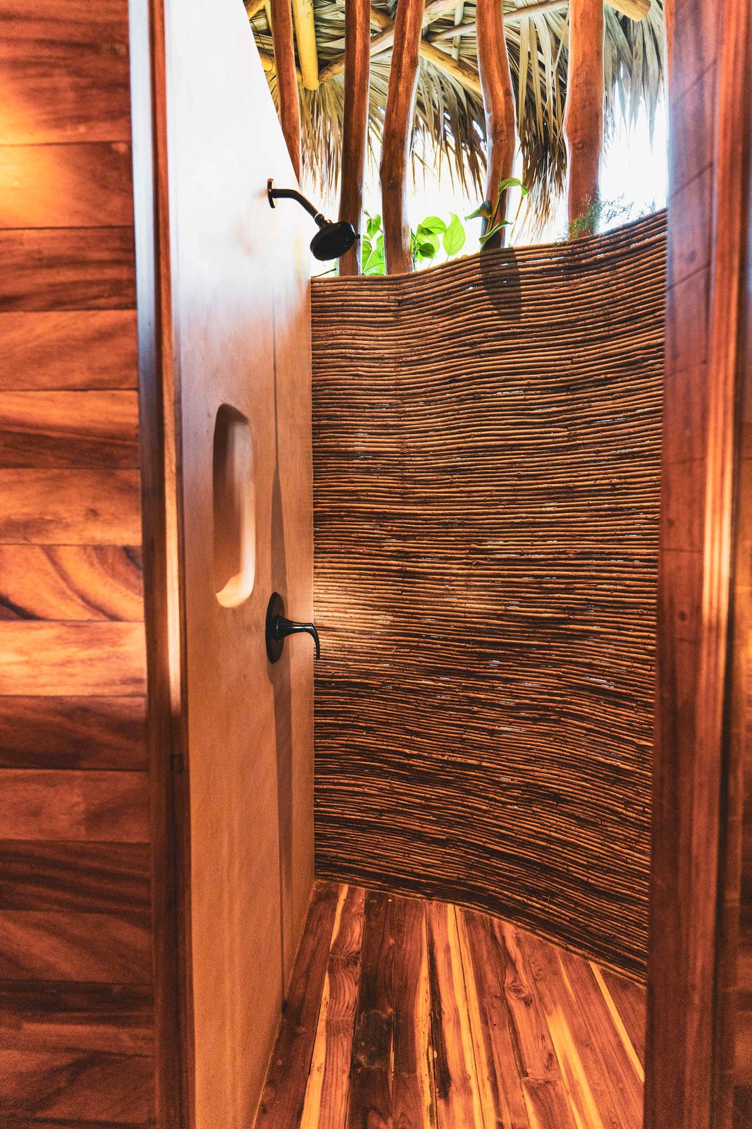An open-air shower walled in woven reed, open to the palms above